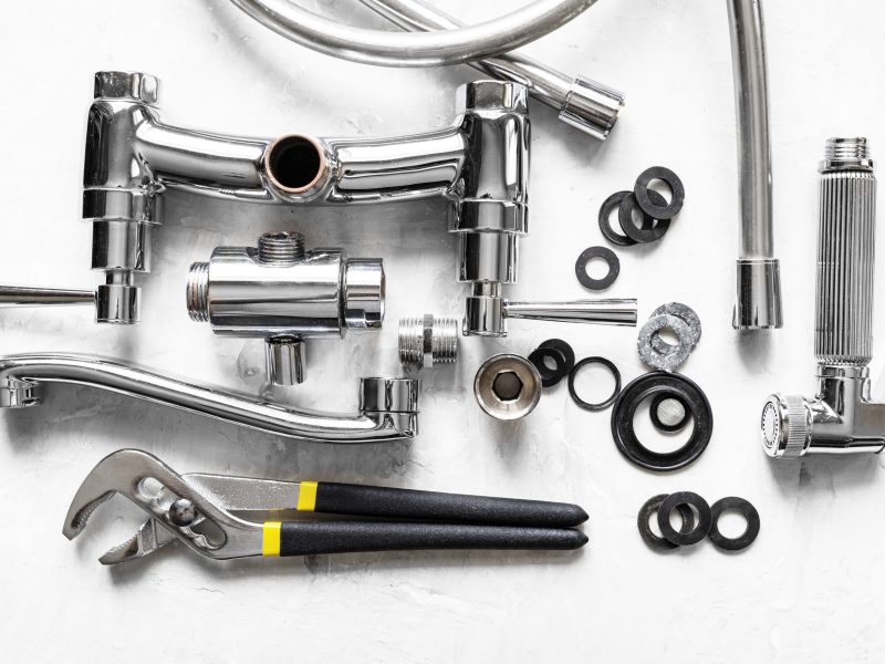 plumbing background - above view of wrench, disassembled shower faucet valve, diverter, spout, hose, various gaskets on concrete board