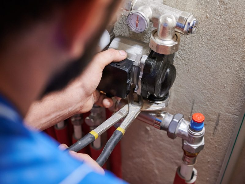Close up of worker hands using wrenches, installing water pump in apartment. Man plumber working on heating system installation. Concept of radiator installation, plumbing works and home renovation.